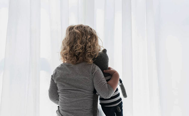 A little girl shown from behind, holding a bear.