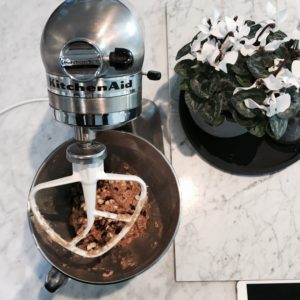 Image of a Kitchen Aid mixer mixing up a cookie dough mixture on a marble work bench.